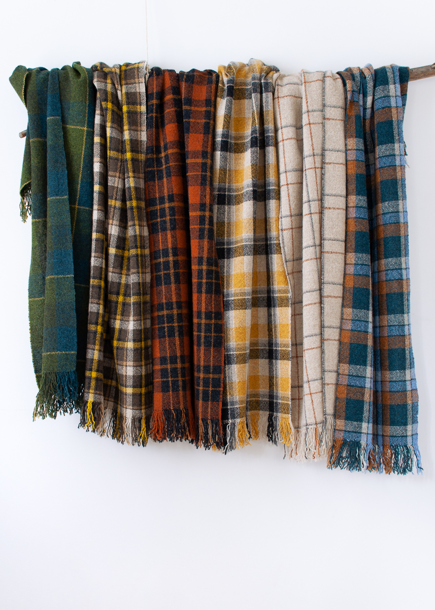 The checkmate scarf collection handwoven by Victoria Pemberton. Six scarves in different check designs hang on a Eucalyptus branch against a white background.